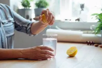 אישה צעירה סוחטת לימון לתוך כוס מים