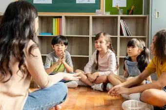 Grundschüler, die auf dem Boden des Klassenzimmers sitzen, hören dem Lehrer zu