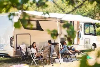 Familie ontspannen op stoelen buiten camper op camping tijdens zomervakantie