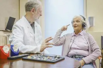 Възрастен пациент, носещ слушалки и разговарящ с аудиолога