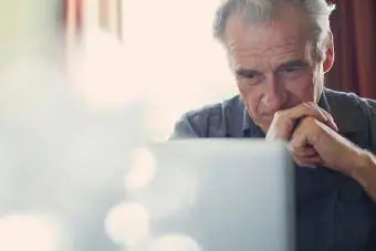 Stariji muškarac sklopljenih ruku koristi laptop