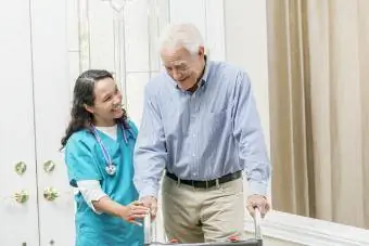 Punonjësja e kujdesit shëndetësor në shtëpi që ndihmon të moshuarin me këmbësor