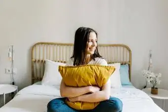 Smaidoša sieviete, kas apskauj spilvenu uz gultas mājās