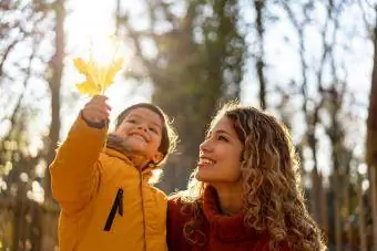Mutter betrachtet ein Blatt, das ihr Sohn an einem sonnigen Herbsttag im Park hält