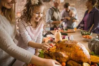 Glückliches Mädchen und ihre Mutter bereiten gebratenen Truthahn für das Thanksgiving-Abendessen zu
