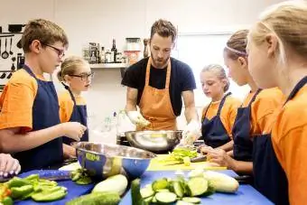 Öğretmen ve öğrenciler yemek pişirme dersinde sebze kesiyor