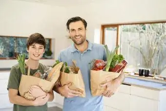 Çocuk ve babası mutfakta alışveriş torbaları tutuyorlar.